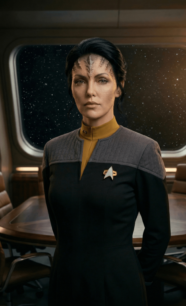 Calpernia Addams as Yh'ahni. Lieutenant Yh'ahni, chief of security, stands with her hands behind her back in the observation lounge aboard the USS Cantabrian-A in 2376. She has skin the color of light clay and rock-like skin growing over her forehead.